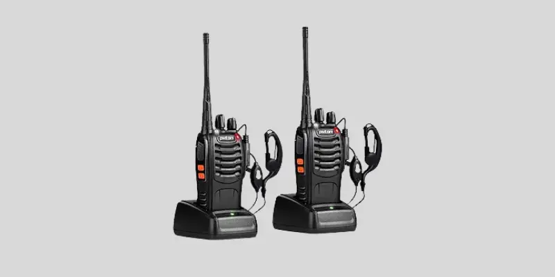 "Two black Pixton two-way walkie talkie devices with 50-mile range, each placed on a charging dock with earpieces attached."