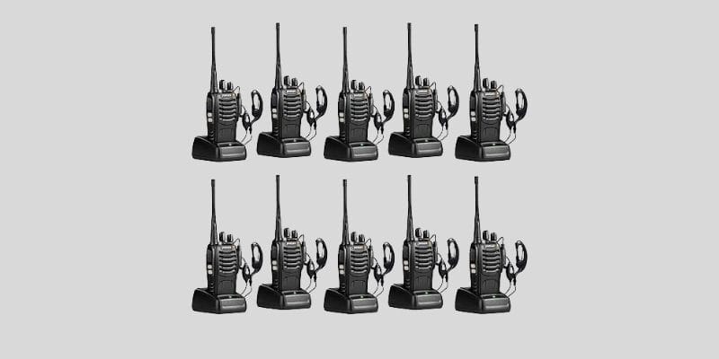 A set of ten black two-way radios with antennas, each placed on a charging dock, accompanied by earpieces, arranged on a gray background.
